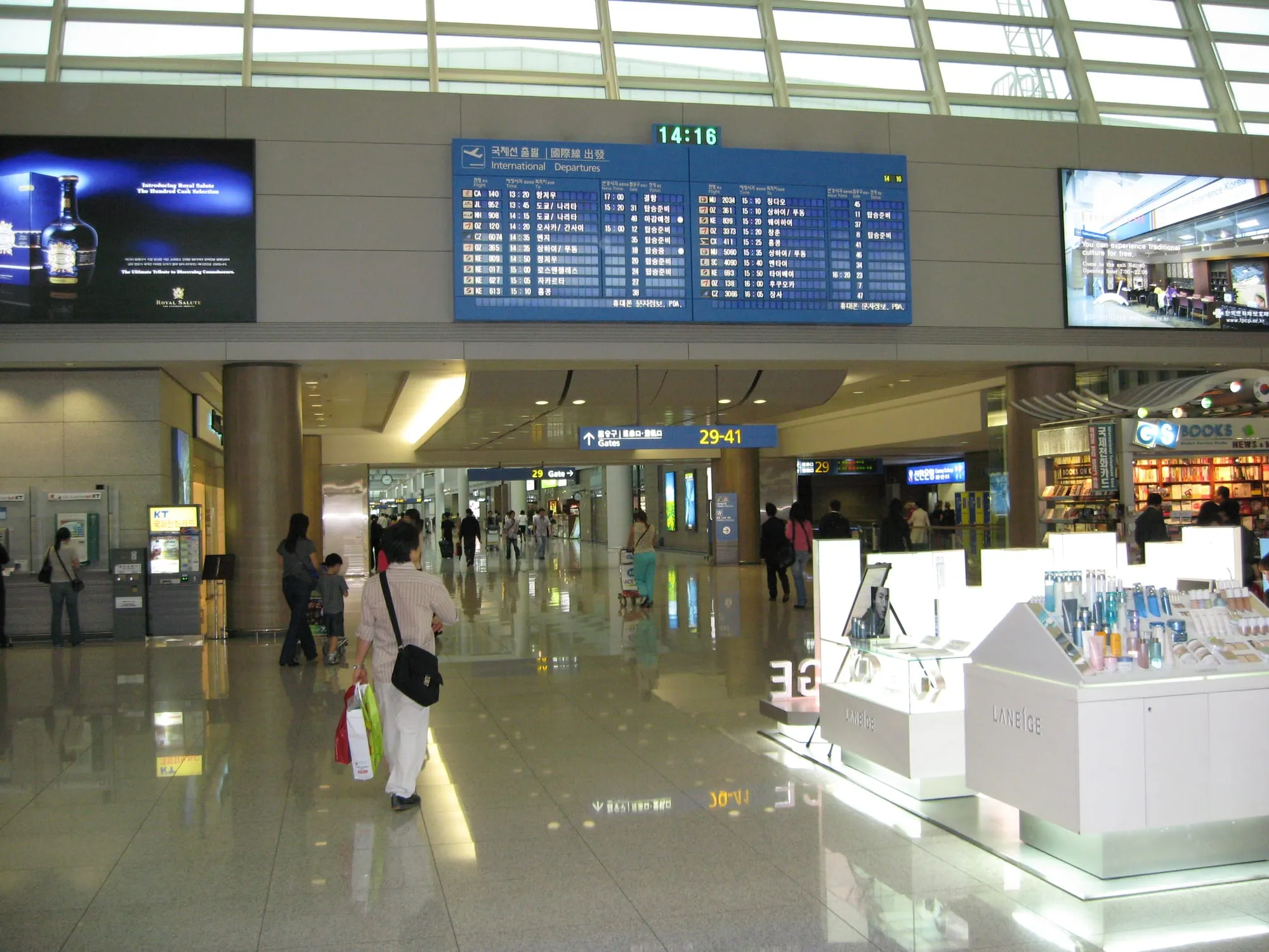 Incheon Airport departures area with a flight board, cosmetics counter and a traveler carrying shopping bags